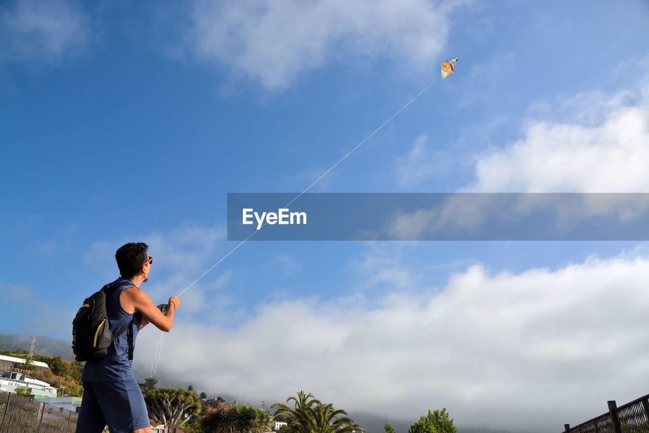 Low angle view of man flying kite against sky