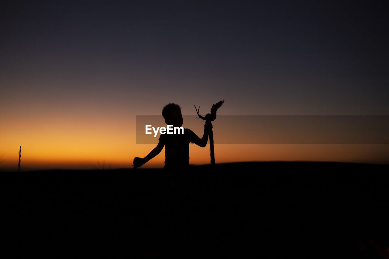 Silhouette of young child standing  against sky during sunset