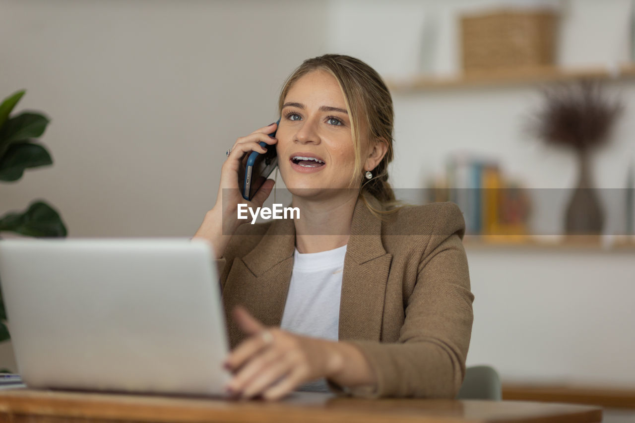 Woman working at home with laptop and speaking on mobile phone. home office. gray notebook 