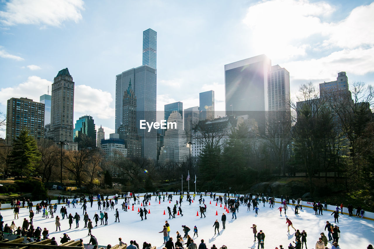 People ice skating by modern buildings against sky