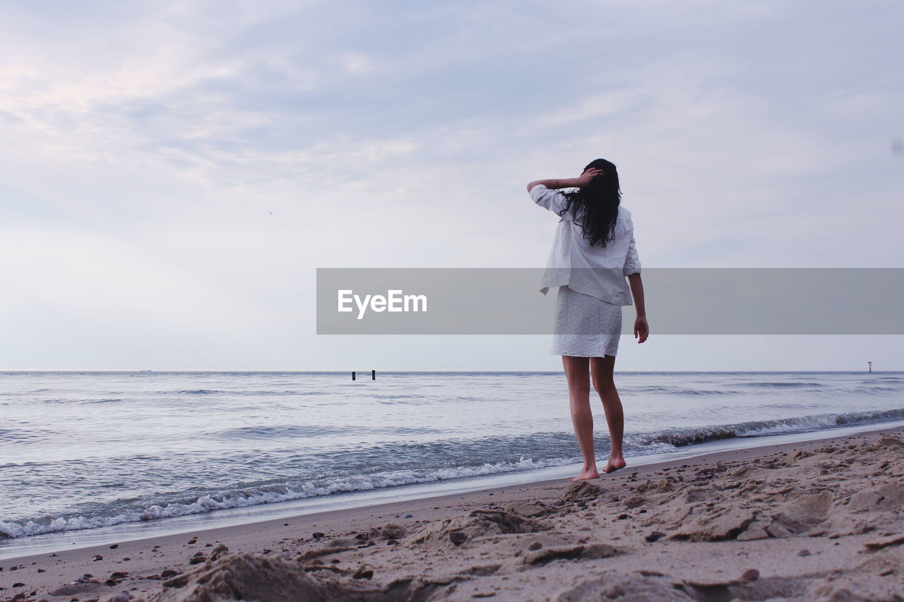 WOMAN STANDING ON BEACH AGAINST SEA