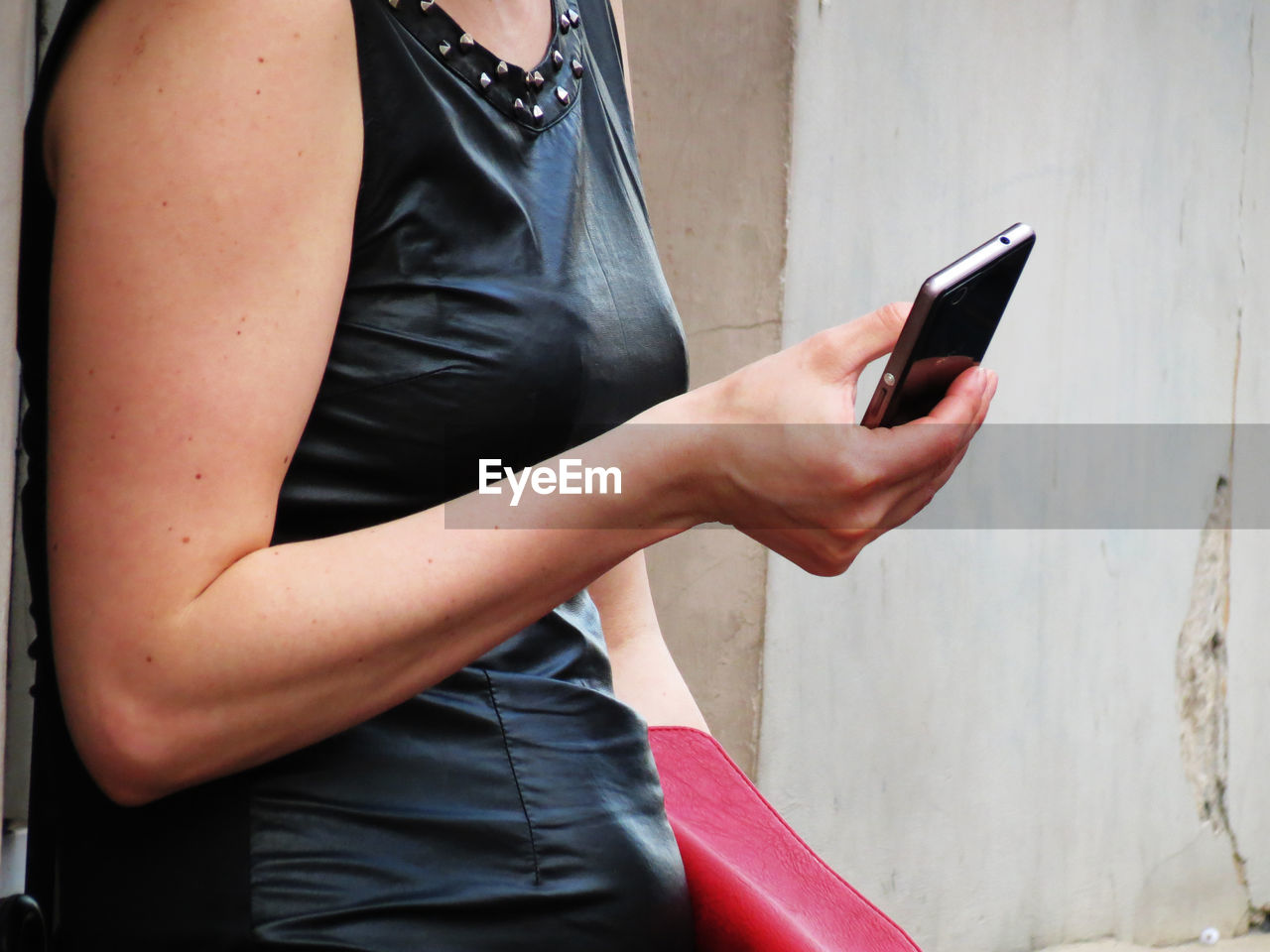 Midsection of woman using mobile phone while standing by wall