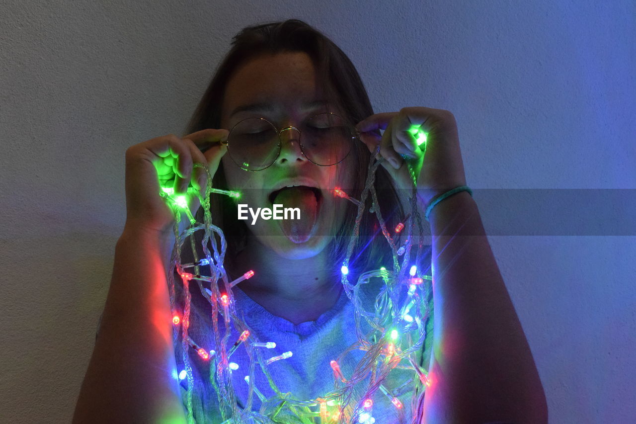 Young woman sticking out tongue with multi colored string lights in darkroom