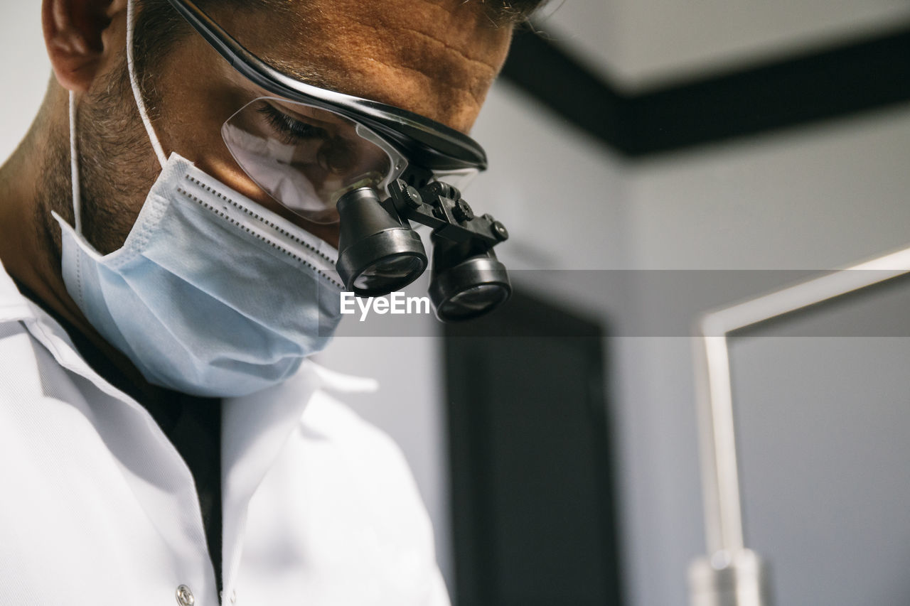 Male dentist wearing mask and surgical loupes while working in clinic