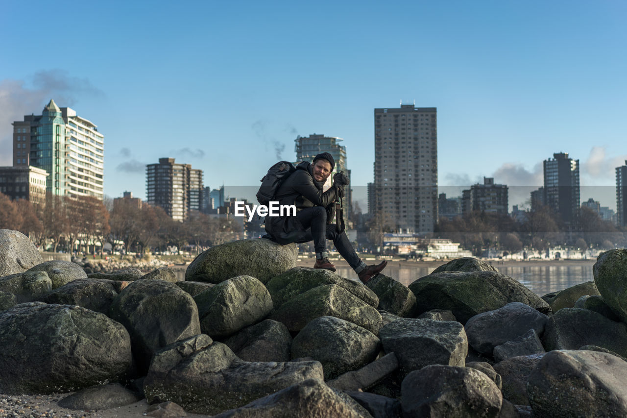 Full length of man sitting on rocks against blue sky