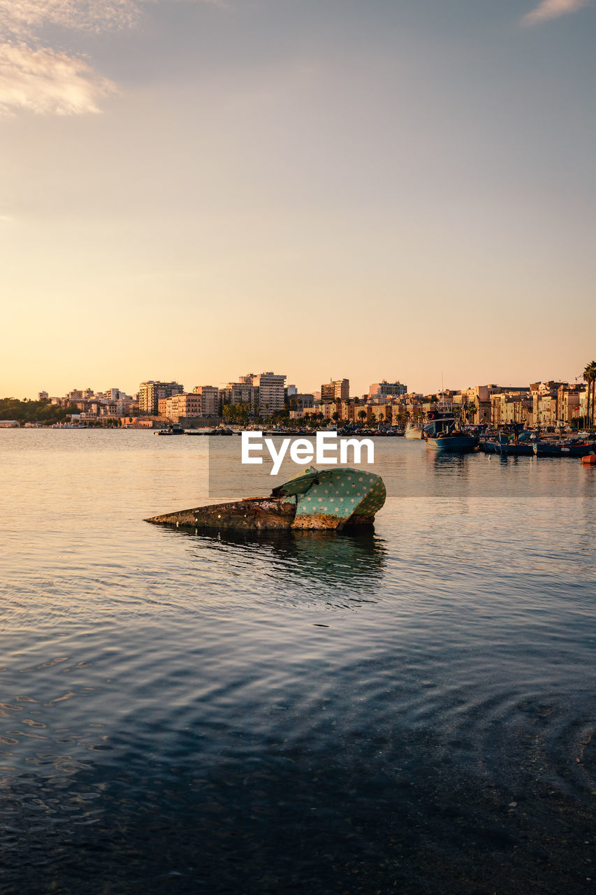 Boat sunk in the port of taranto vecchia with the city of taranto behind it