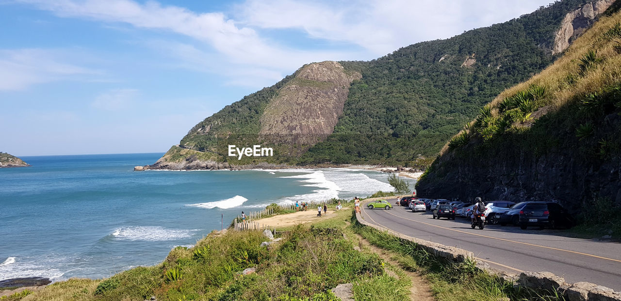 Scenic view of road amidst sea and mountain against sky