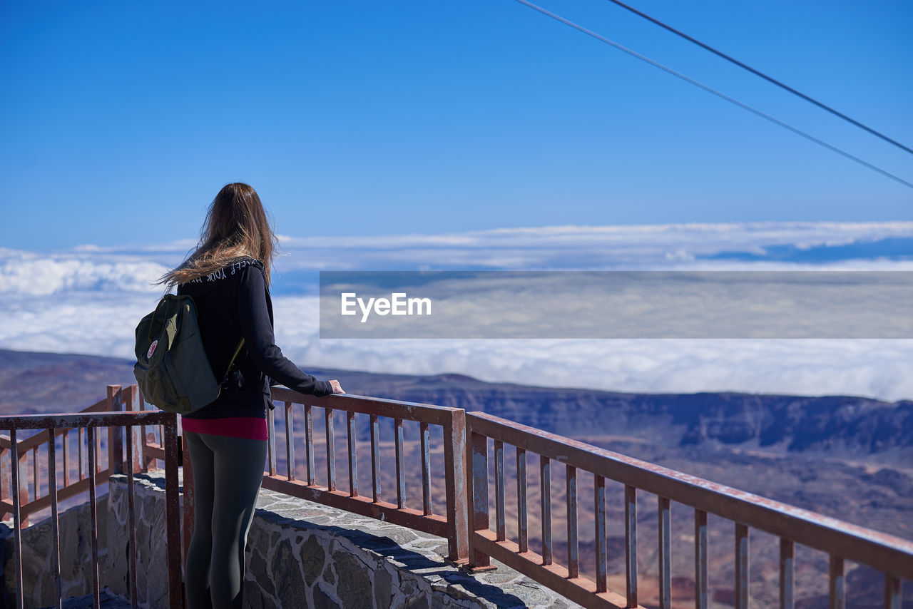 Woman standing by railing against sky