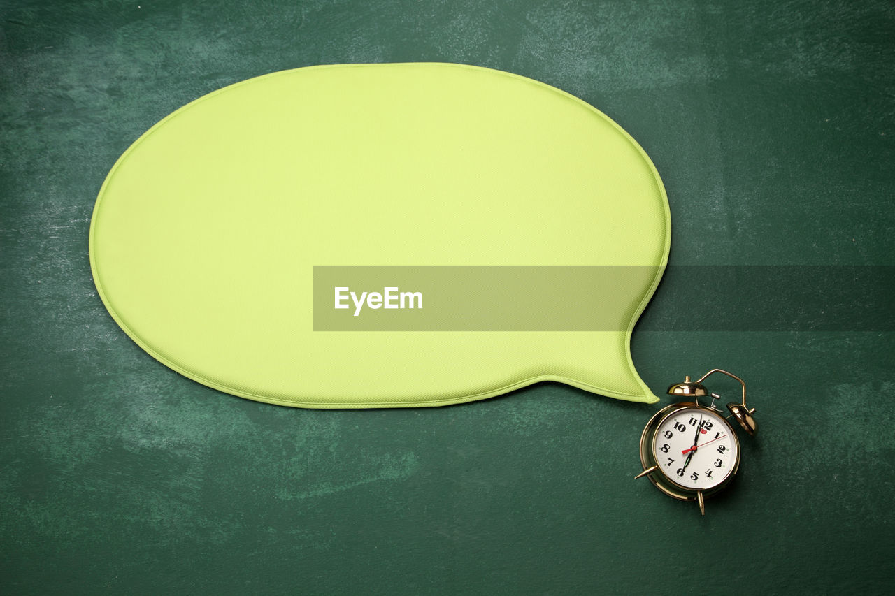 High angle view of blank green speech bubble with alarm clock on blackboard