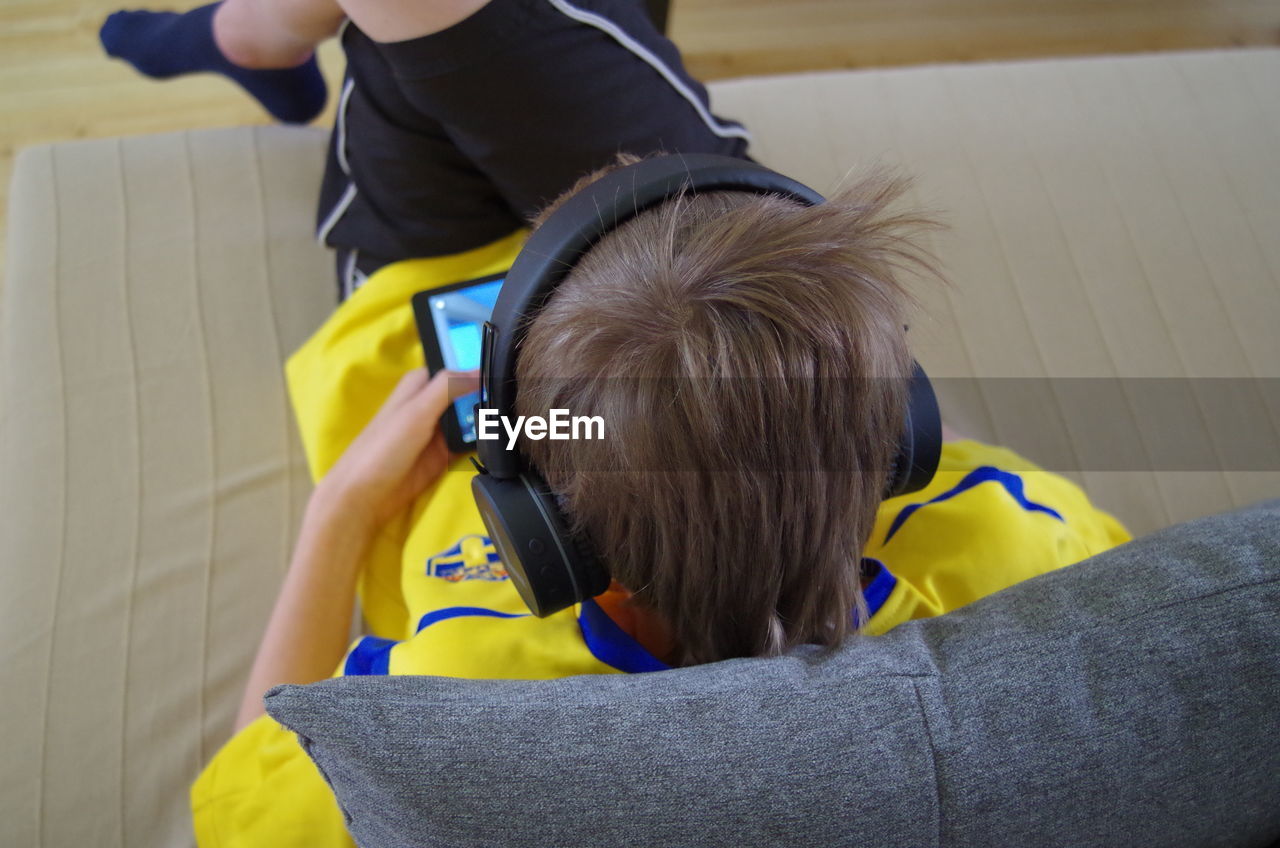 High angle view of boy playing video game while sitting on sofa at home