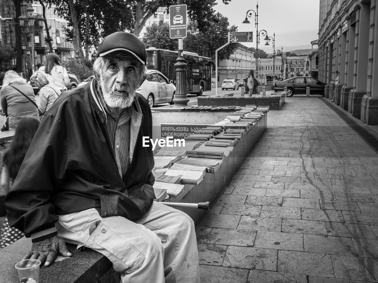 MAN SITTING ON STREET AMIDST CITY