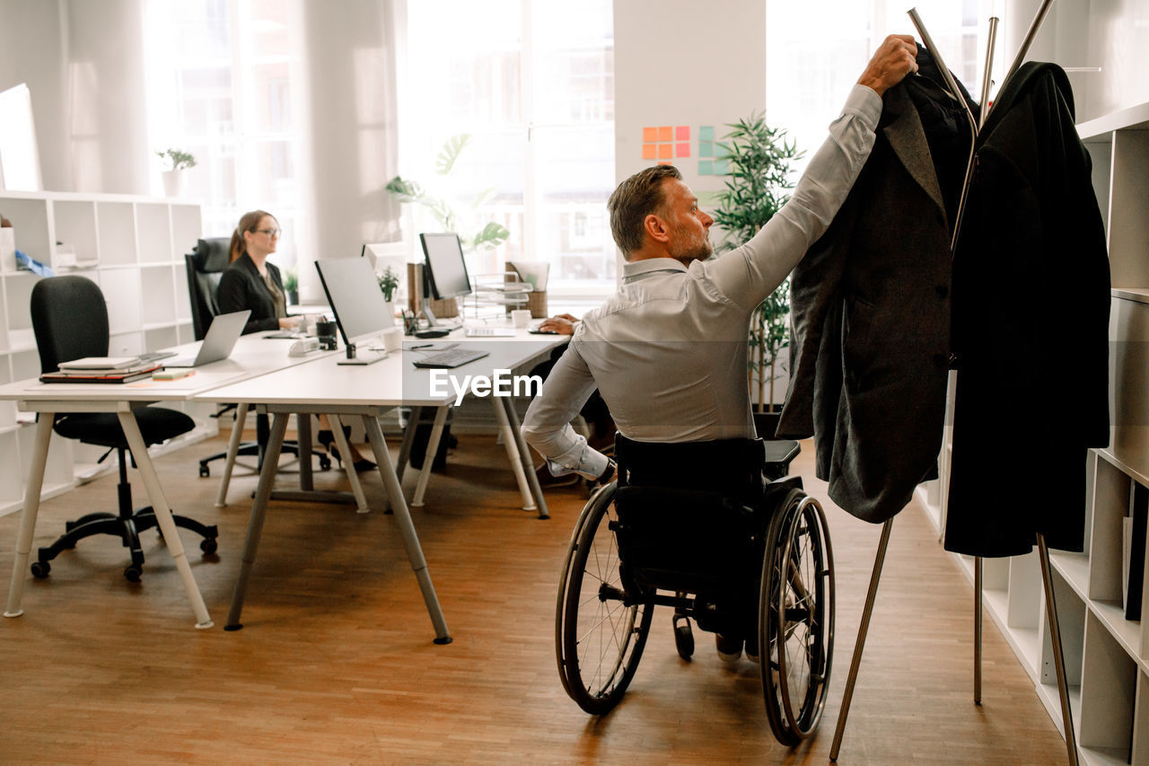 Rear view of disabled businessman hanging coat in office