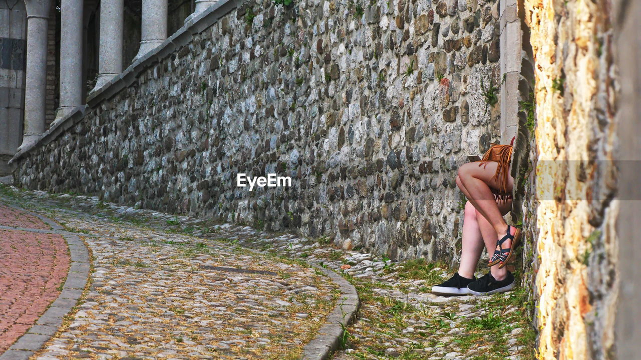 SIDE VIEW OF WOMAN WALKING ON WALL BY BUILDING