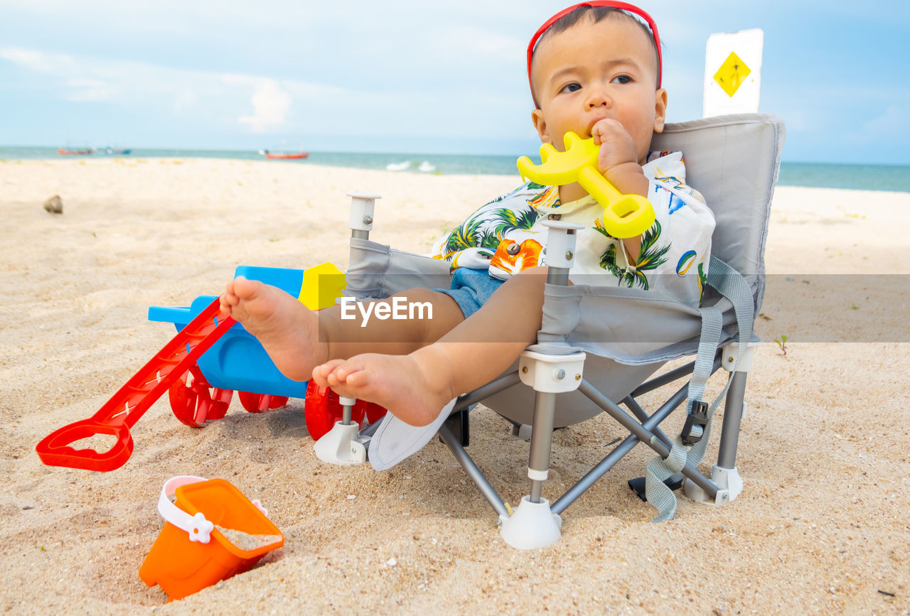 BOY SITTING ON CHAIR AT SHORE