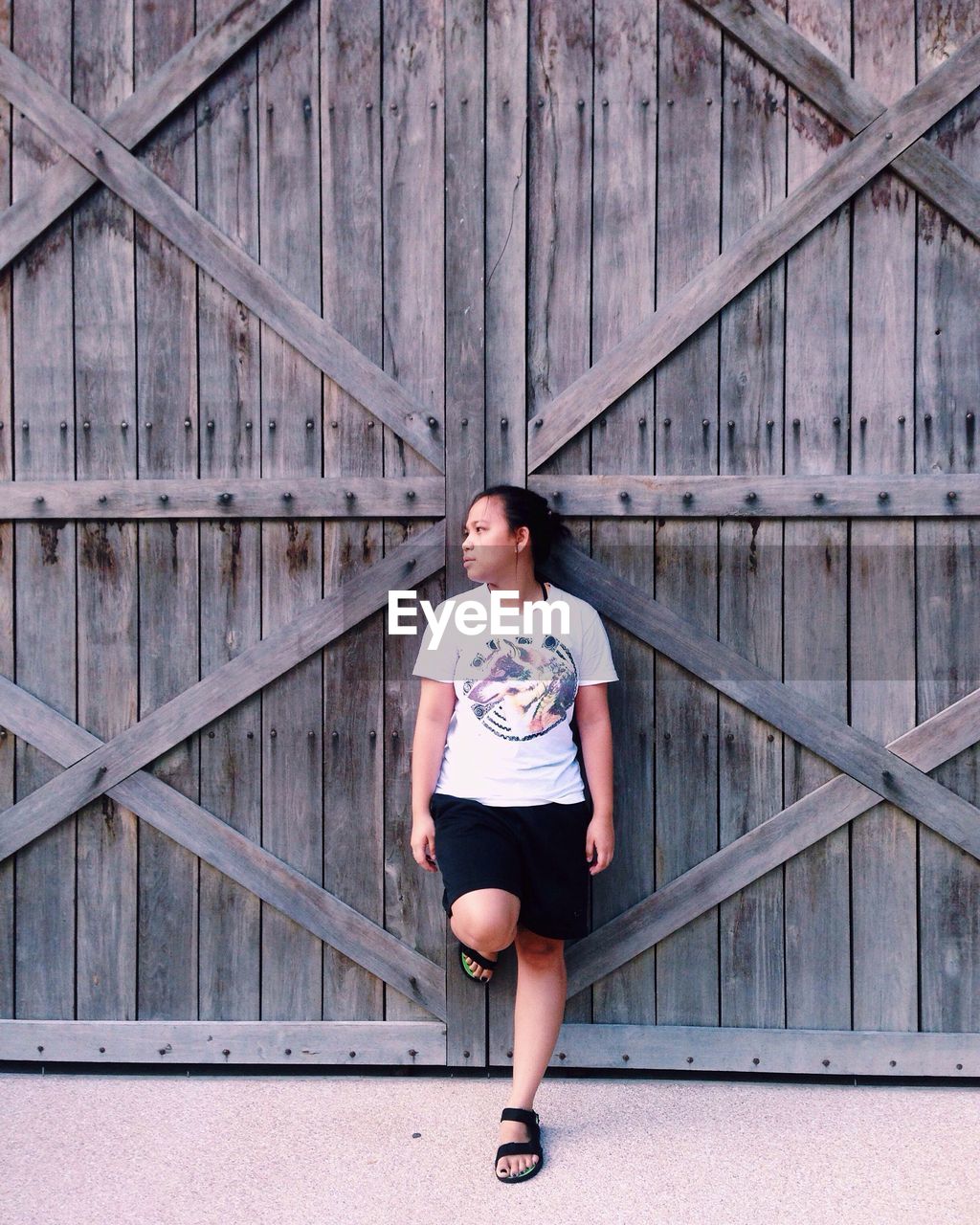 Full length of young woman standing against wooden wall