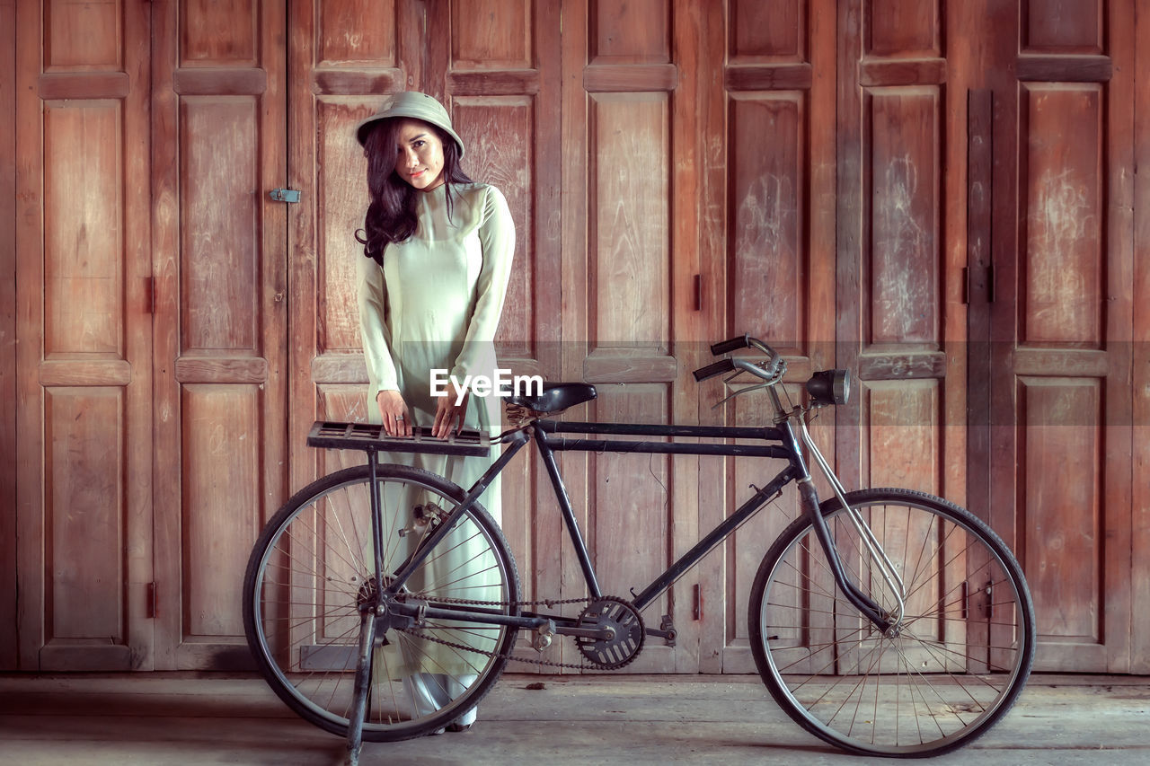 Portrait of young woman standing by bicycle on street