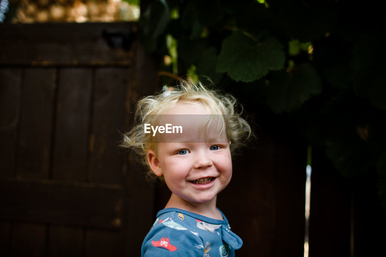 Blond two year old boy smiling for camera standing in yard