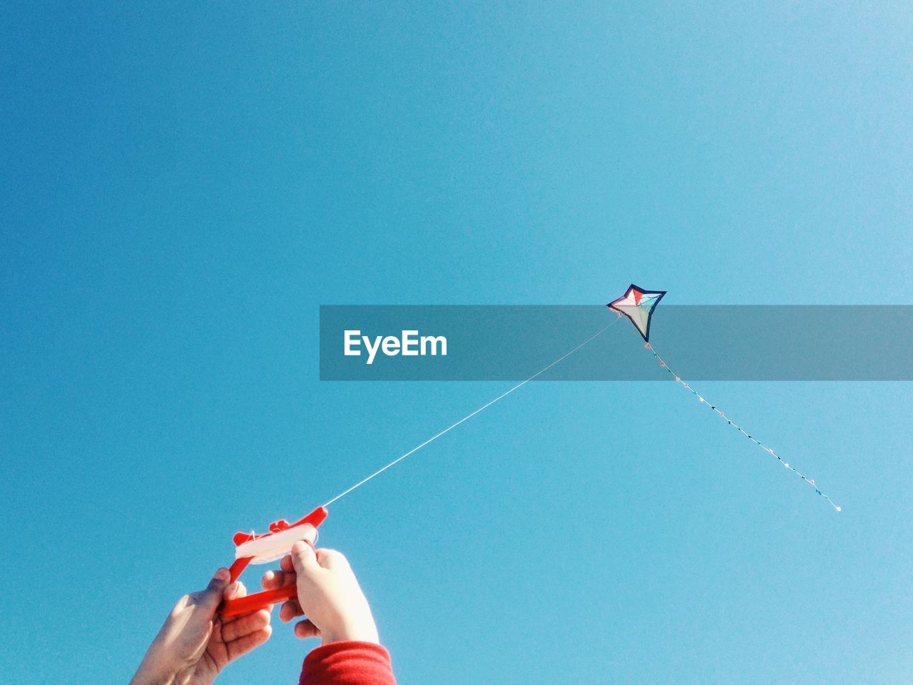 Close-up of hands flying kite against clear blue sky