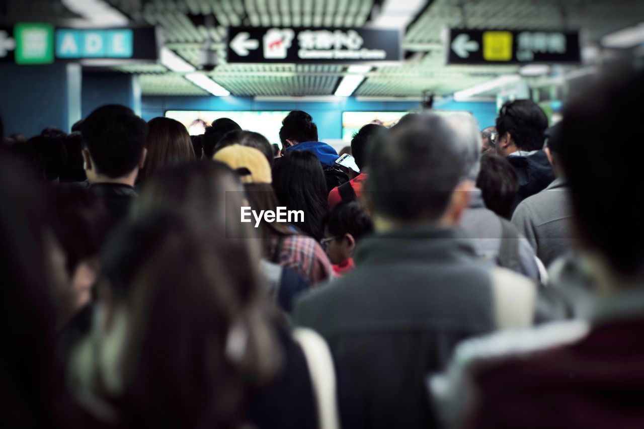 Back portrait crowd of people walk in the subway station during rush hours with blurred sign boards