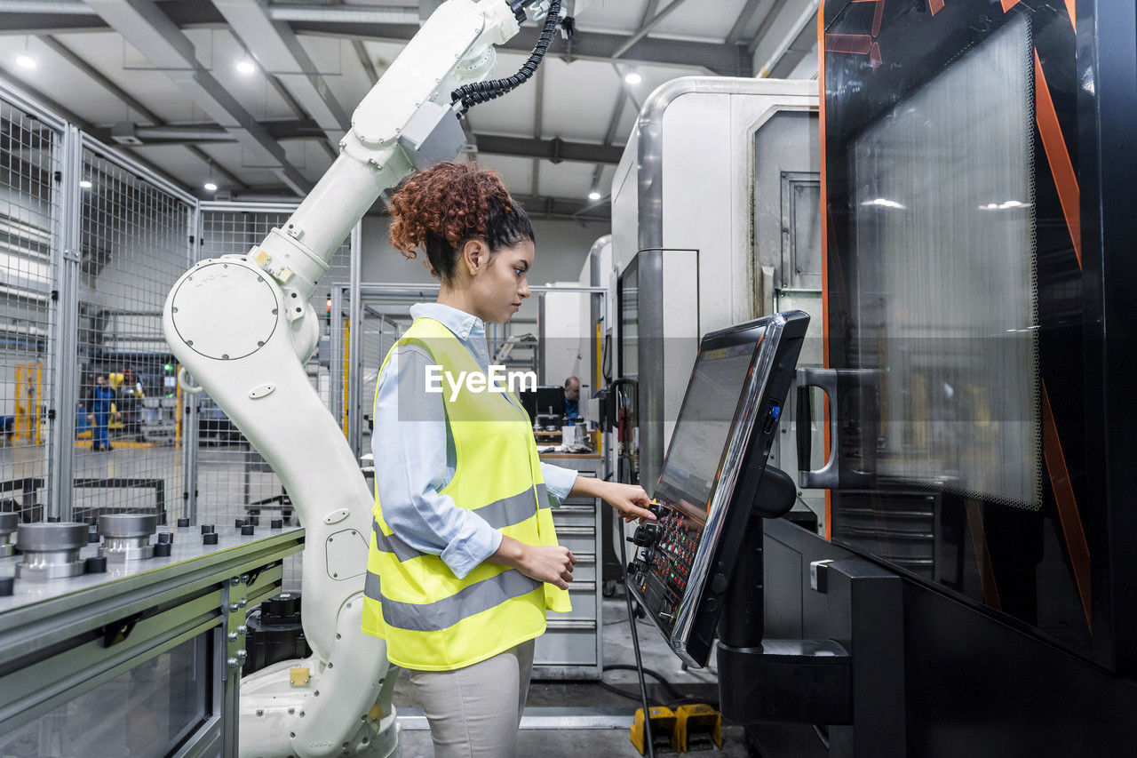 Engineer standing by robotic arm and operating machine in factory