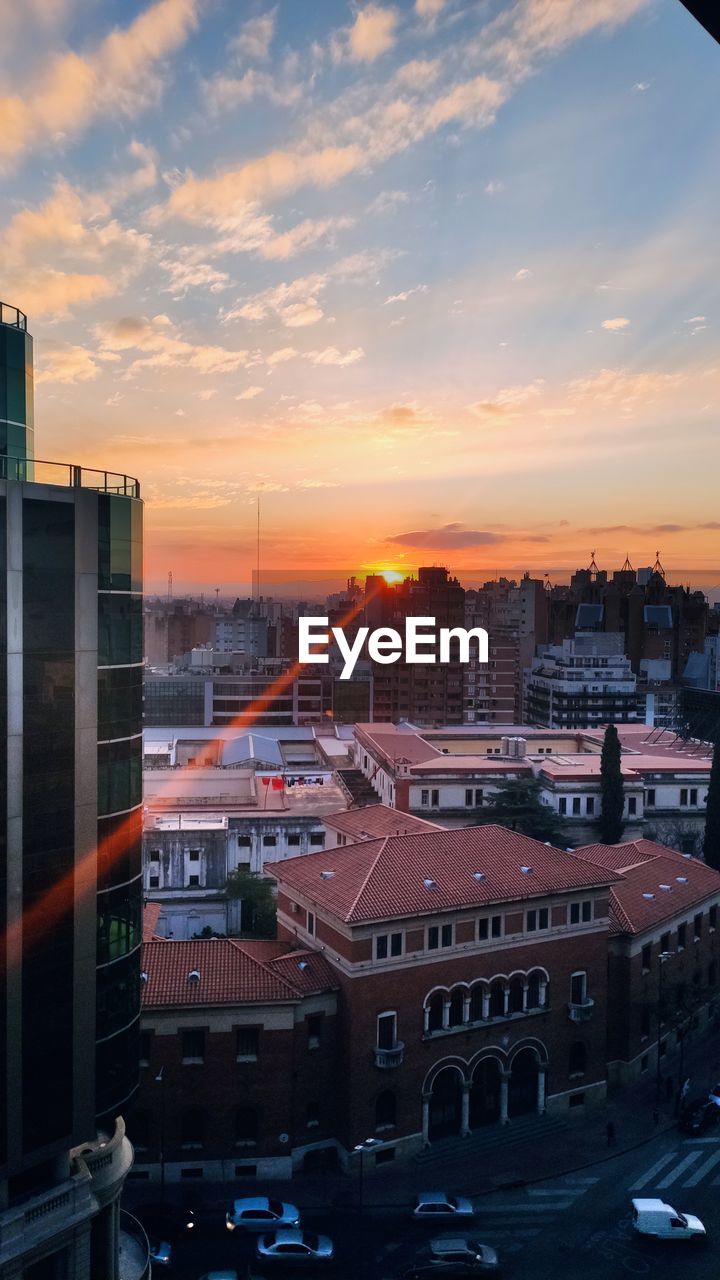 HIGH ANGLE VIEW OF STREET AMIDST BUILDINGS AGAINST SKY DURING SUNSET