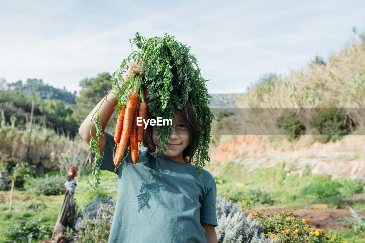 Boy standing in vegetable garden, holding a bunch of carrots