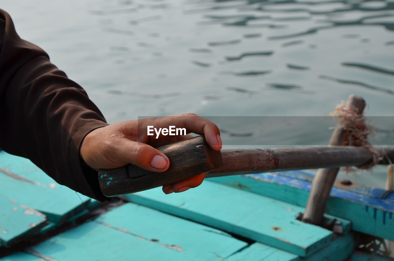 Cropped hand holding oar on boat in sea