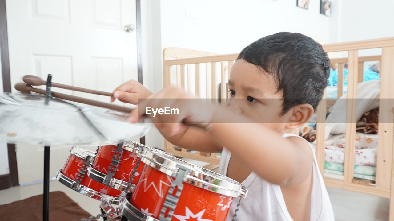 Cute baby boy playing drum kit at home