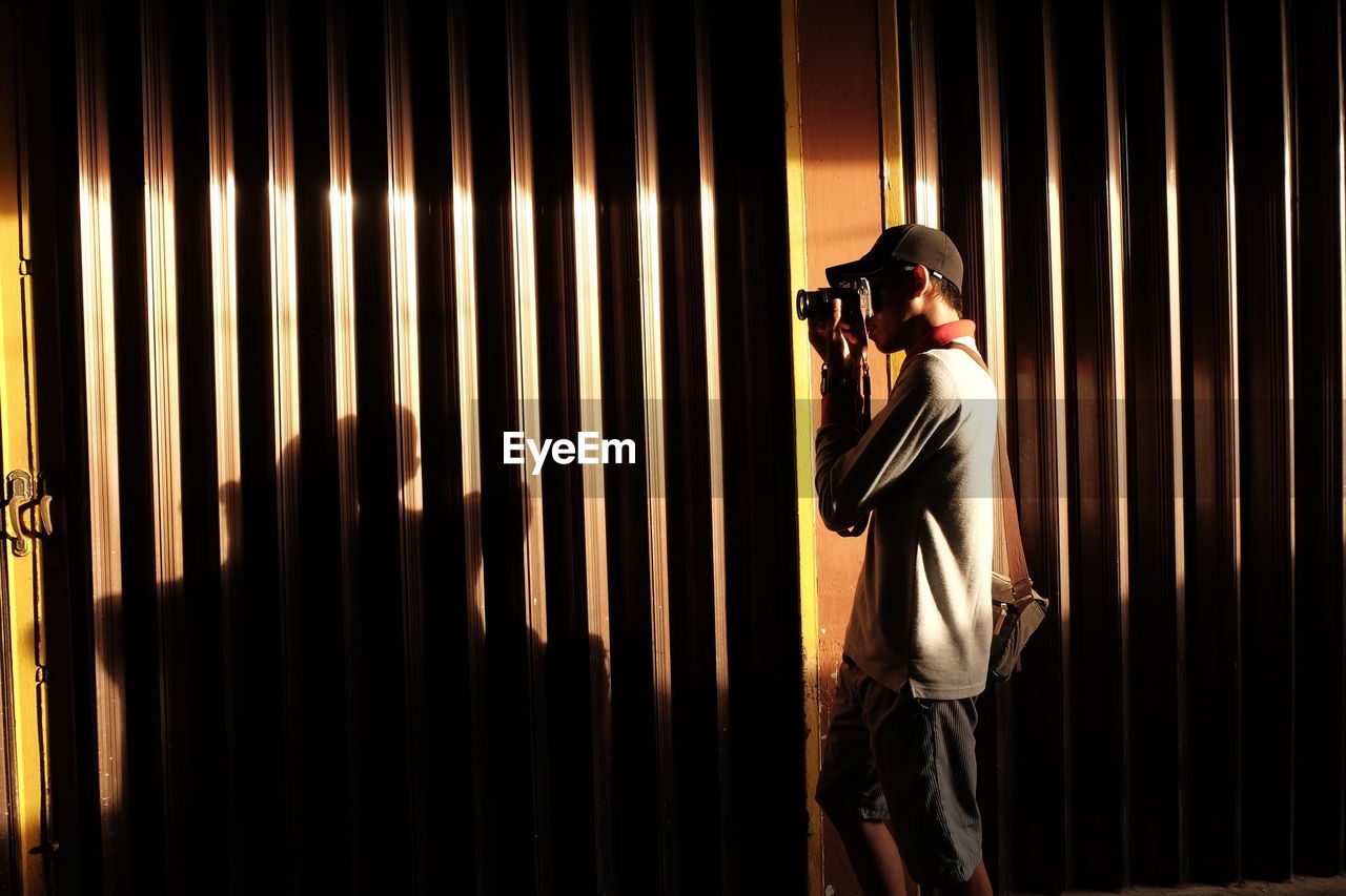 Side view of man photographing through camera while standing by shutter