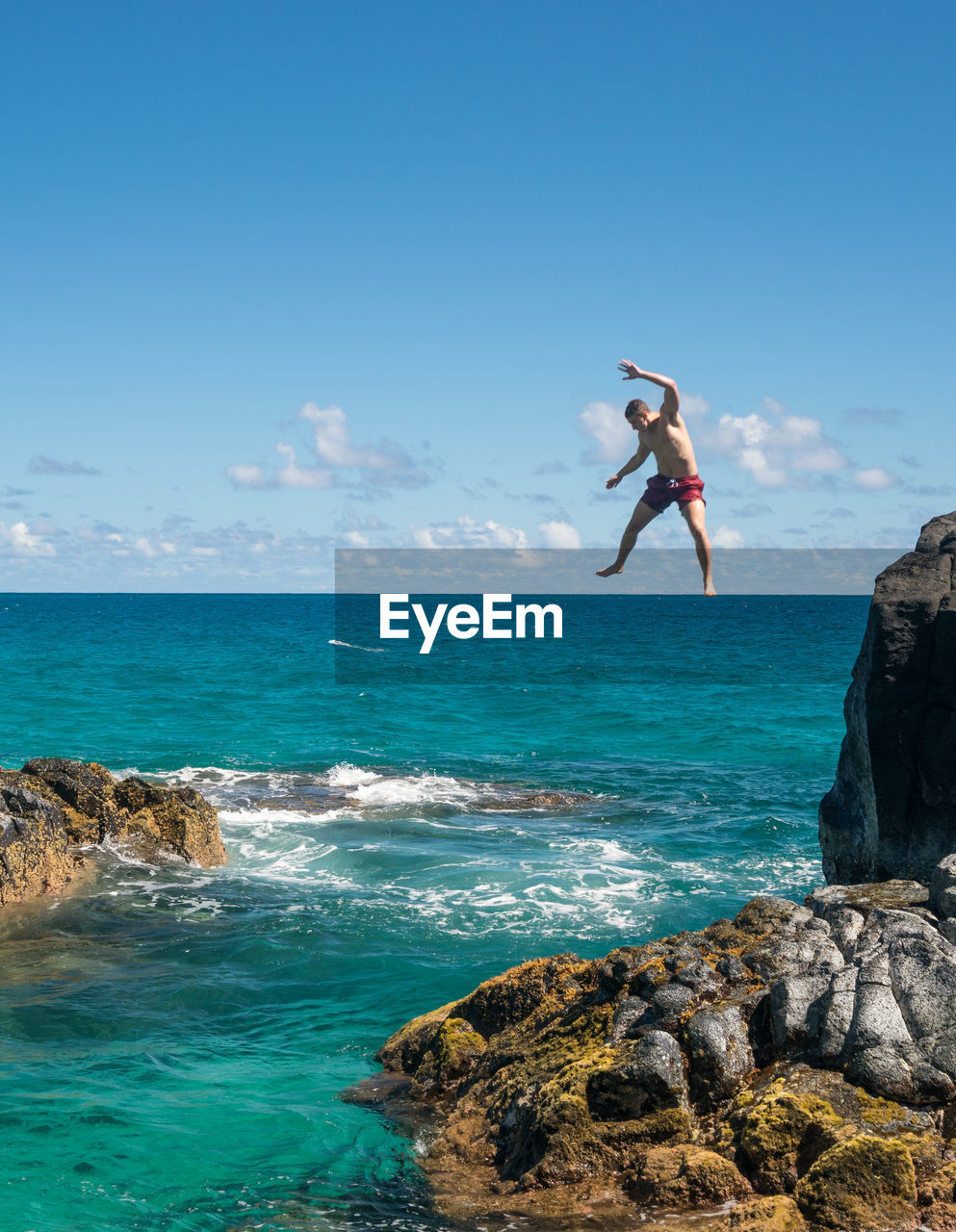 Low angle view of shirtless man jumping in sea from cliff against sky