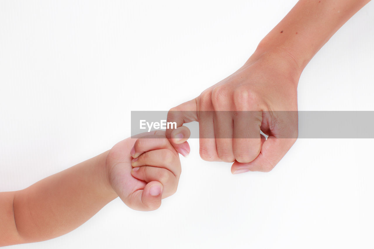 Close-up of hands giving pinky promise over white background