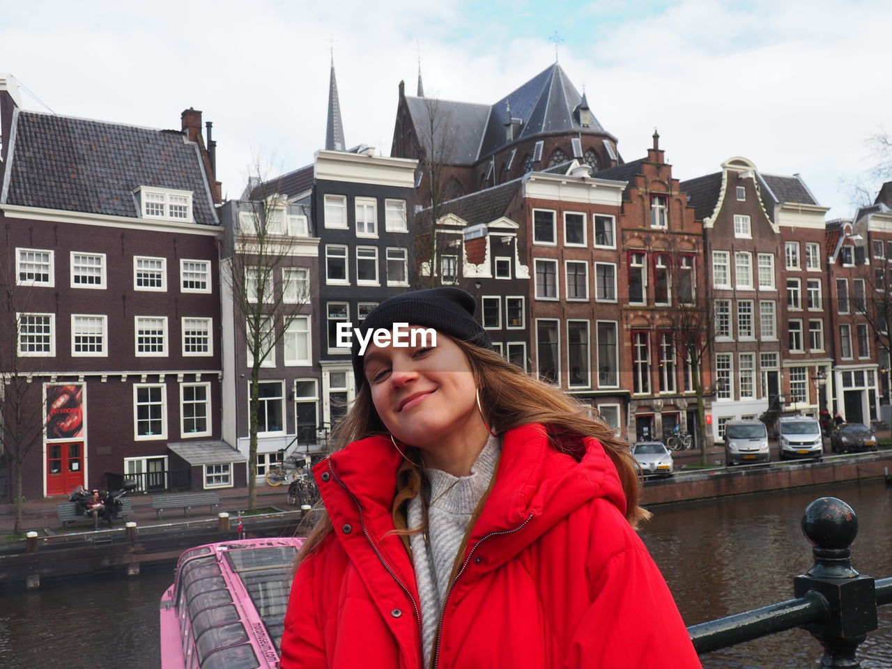 PORTRAIT OF SMILING YOUNG WOMAN STANDING AGAINST BUILDINGS