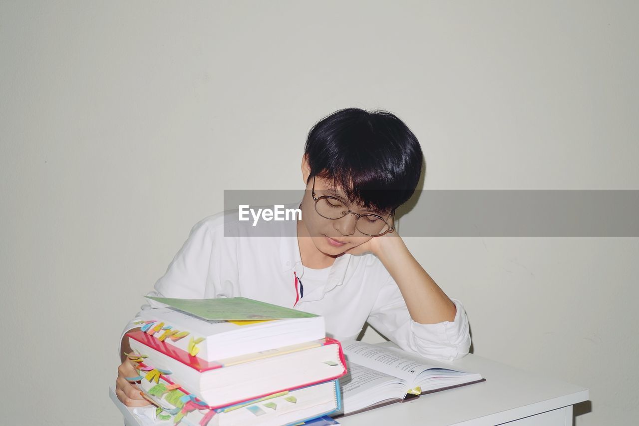 Young woman sitting with head in hand by table with book against white background