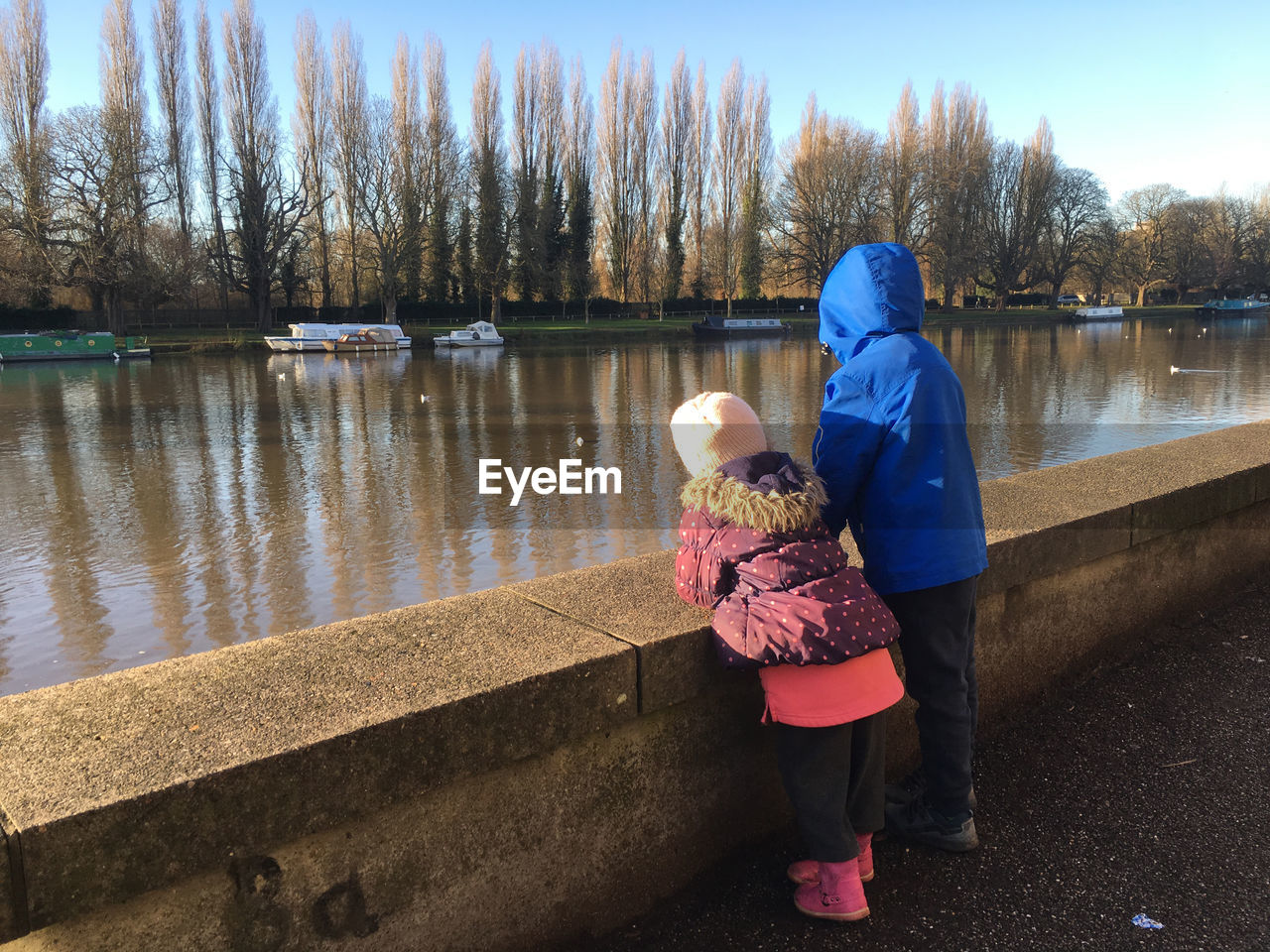 REAR VIEW OF MOTHER AND SON STANDING BY RIVER