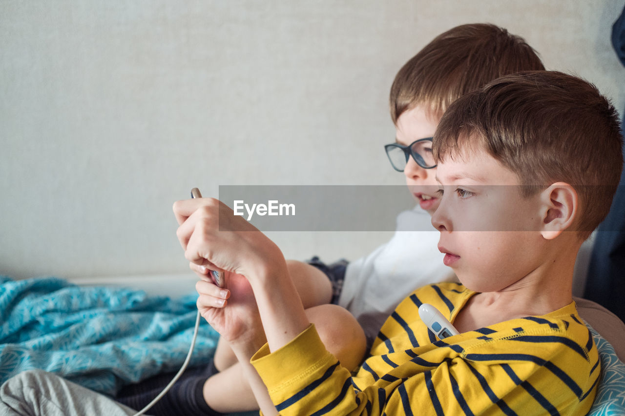 Two boys are lying on the bed, on sick leave with a thermometer under their armpit 