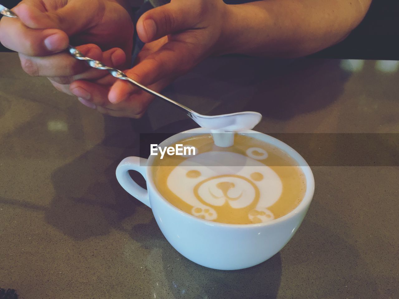 Cropped image of person making teddy bear art on cappuccino