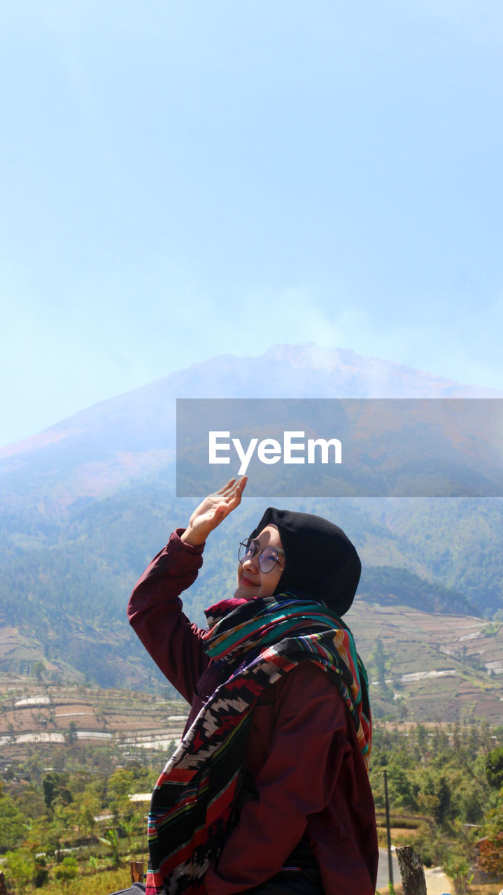 Woman shielding eyes while standing on mountain against sky