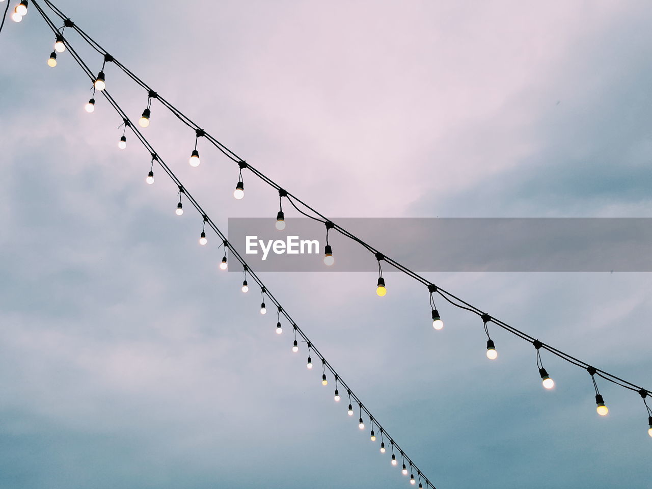 Low angle view of light bulbs hanging against sky