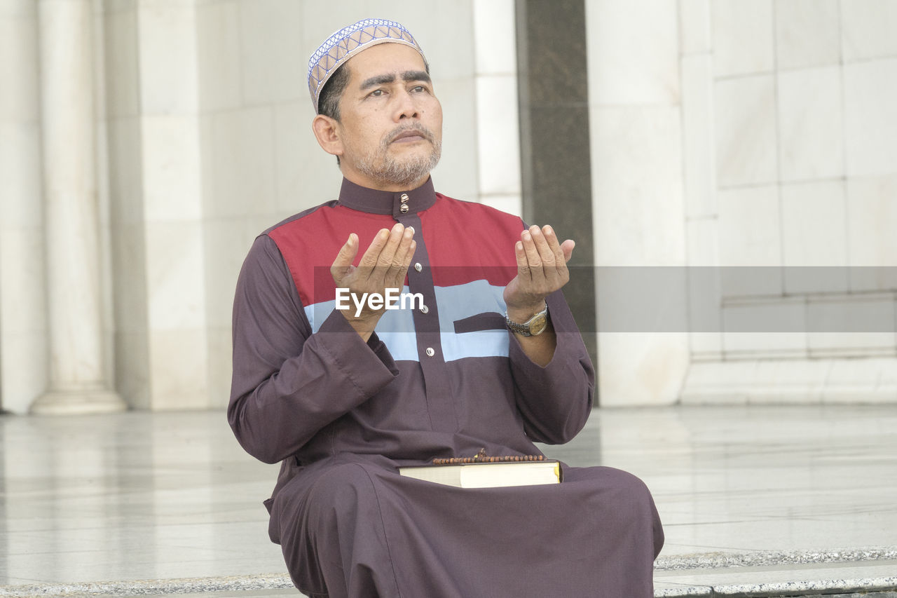 Mature man praying while sitting at mosque