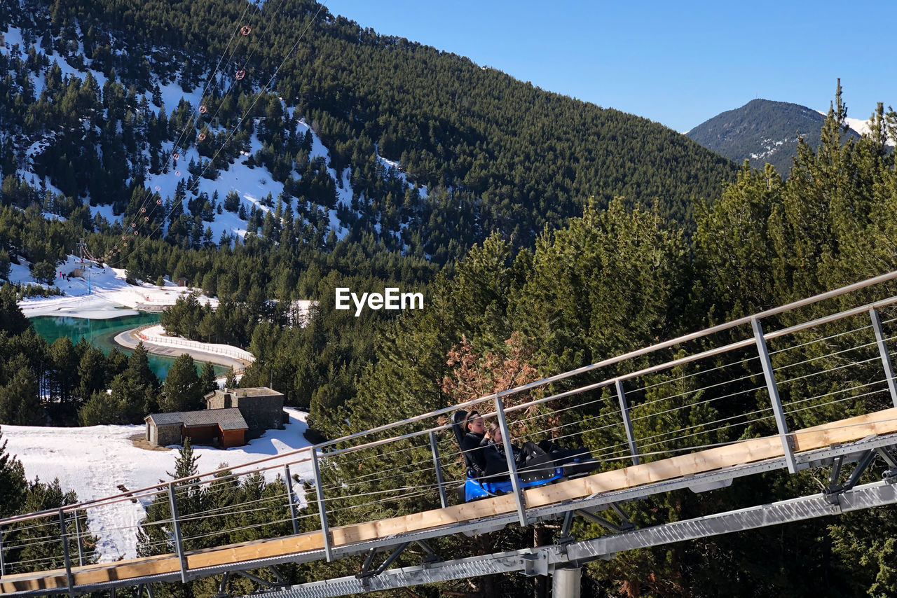 PEOPLE ON FOOTBRIDGE AGAINST MOUNTAIN RANGE