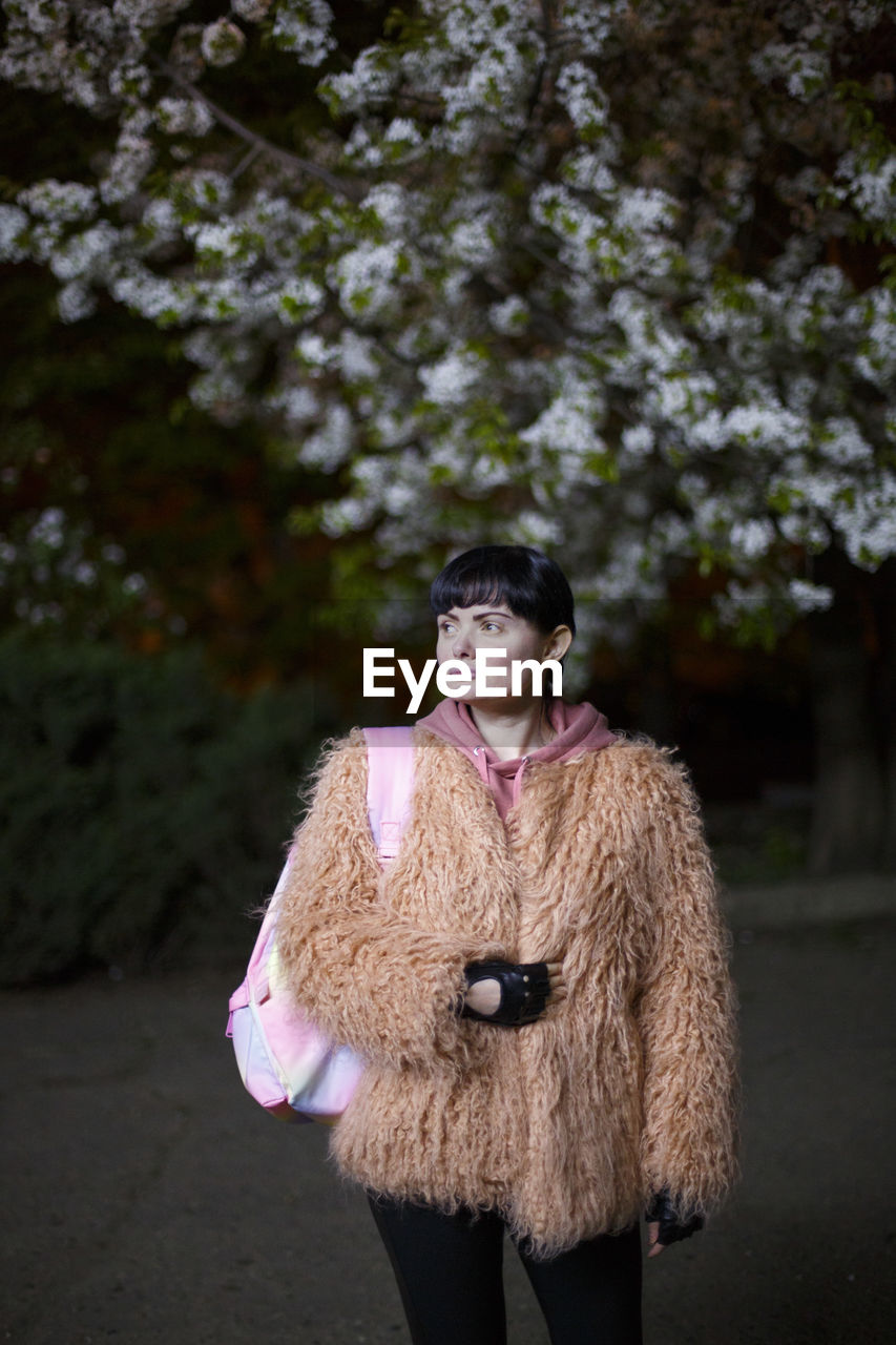 WOMAN LOOKING AWAY WHILE STANDING AGAINST TREES