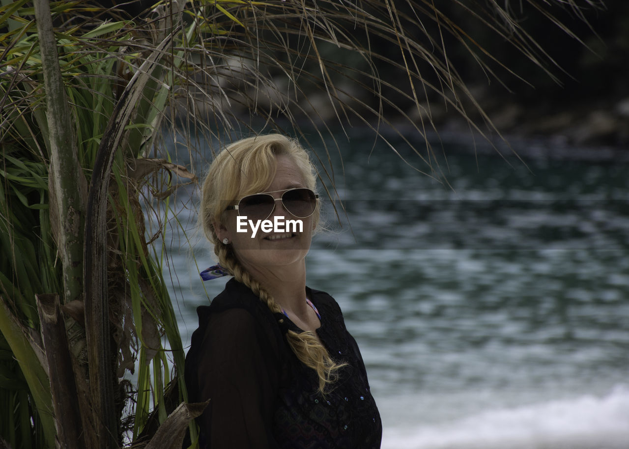 Portrait of young woman against palm tree at beach