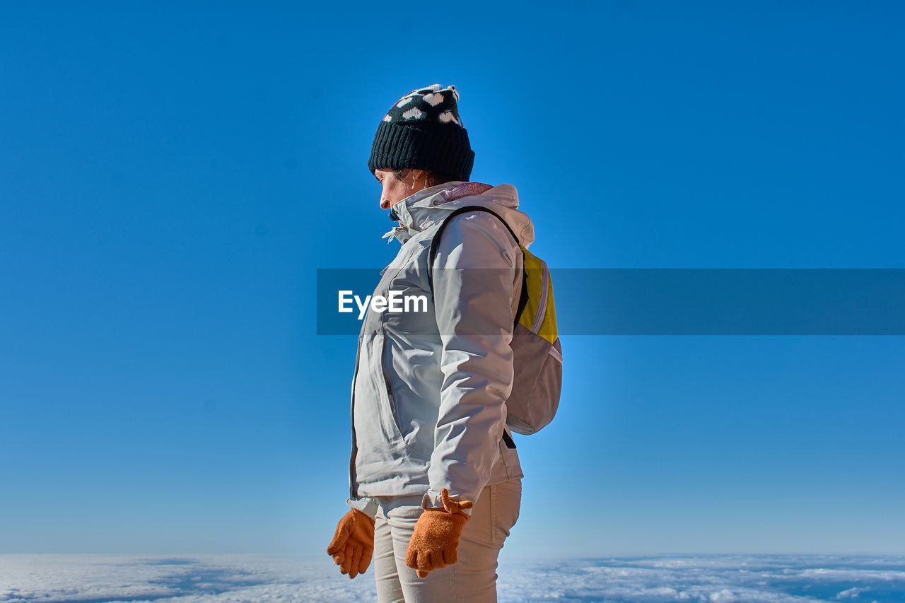 Side view of woman standing against clear blue sky during winter