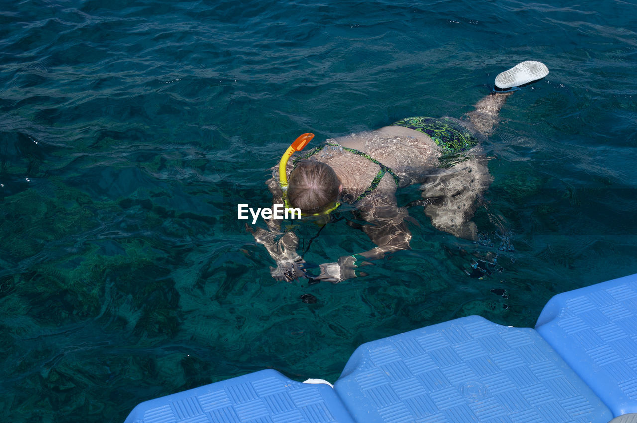 Plump girl in a green swimsuit and a swimming mask, dives and swims in the sea