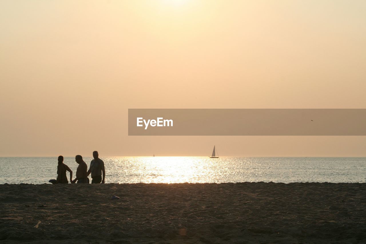 Silhouette people walking at beach during sunset