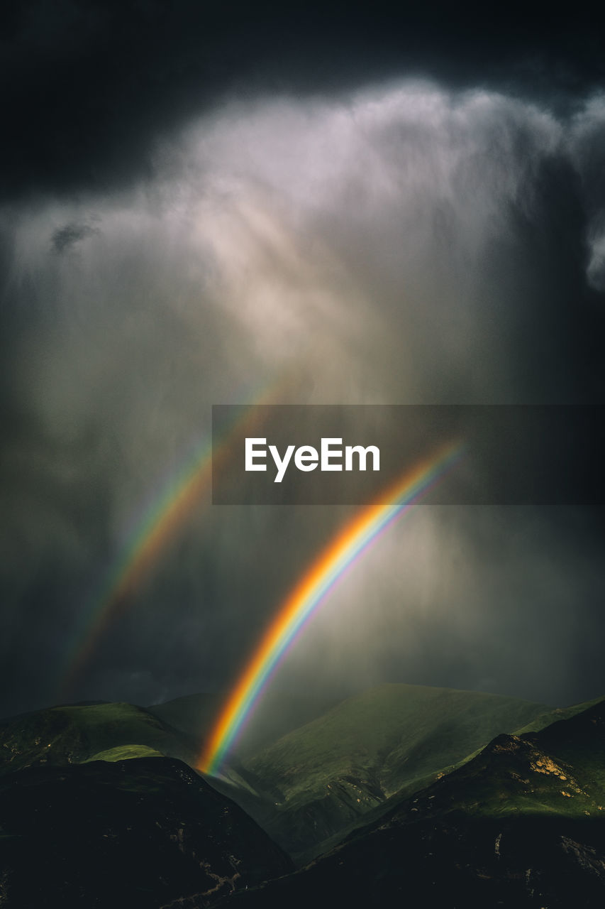 Scenic view of rainbow over mountains against cloudy sky