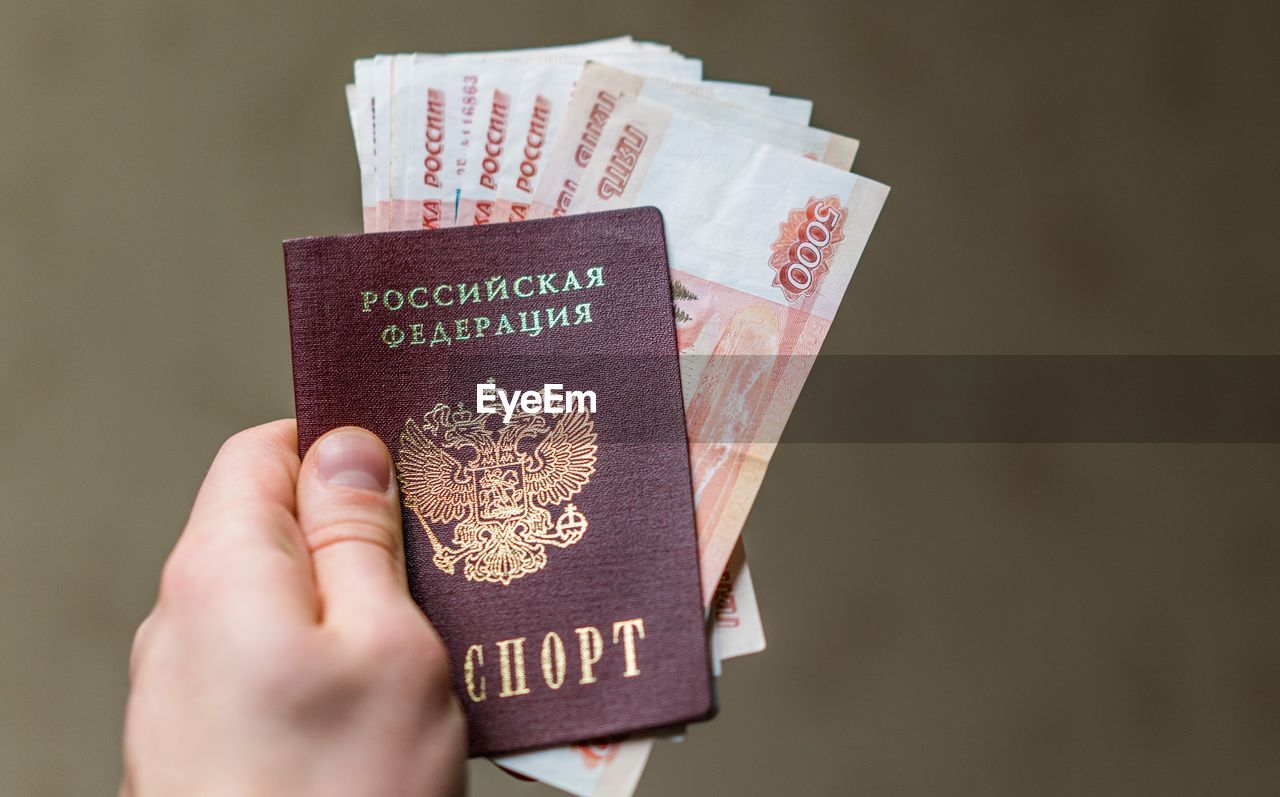 Close-up of man holding money and passport against brown background