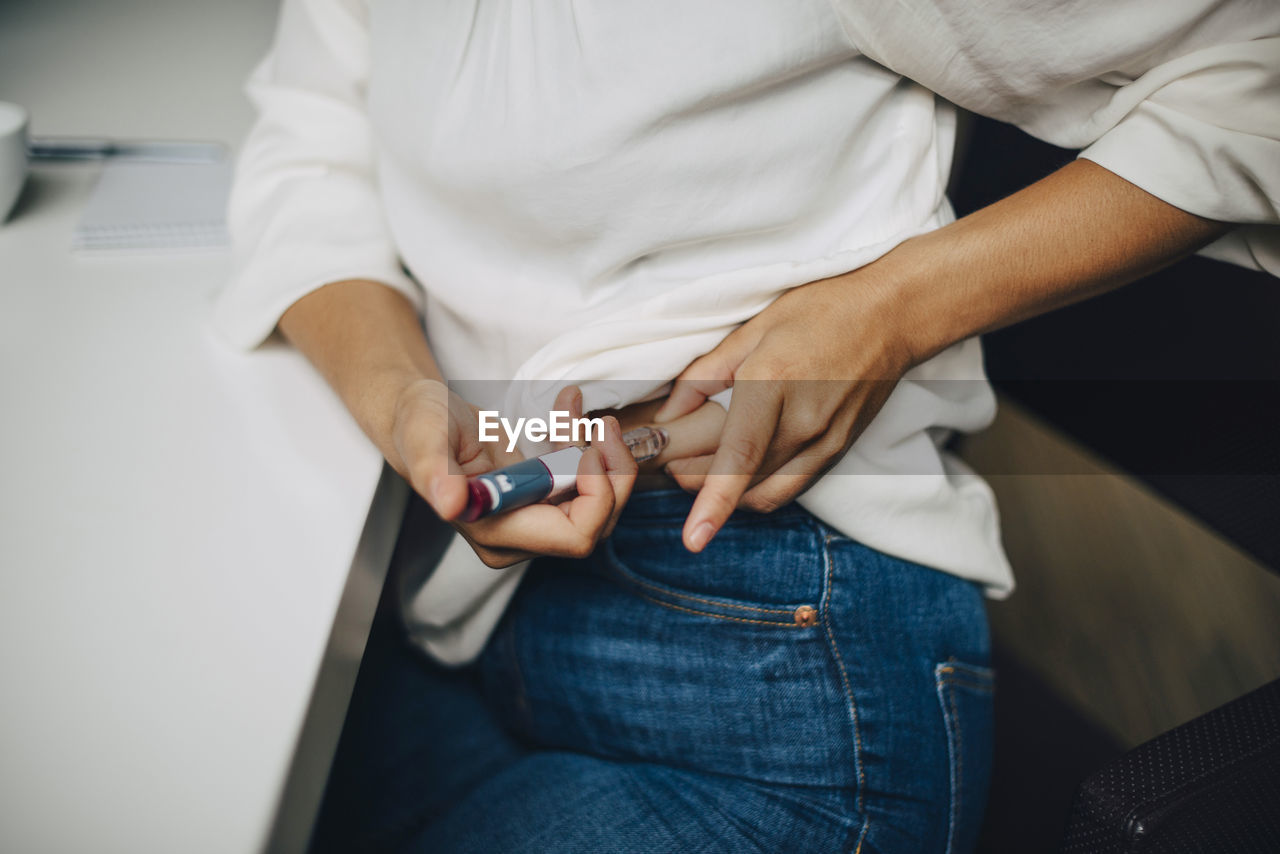 Midsection of businesswoman injecting insulin in abdomen while sitting at table