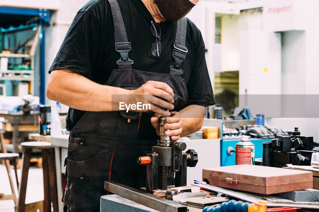 Crop anonymous factory worker wearing uniform working on lathe with drilling machine in contemporary light craftsmanship