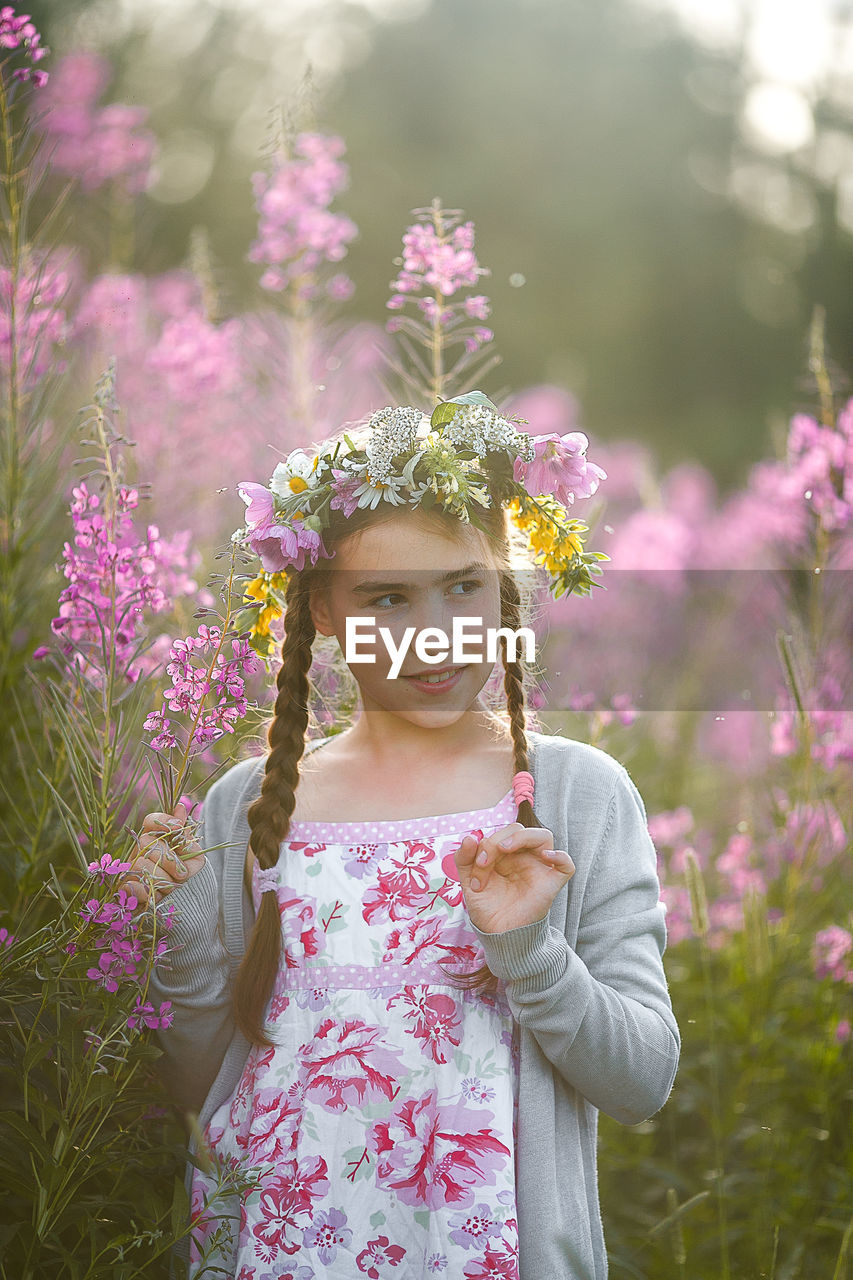 Girl looking away while standing against flowering plant